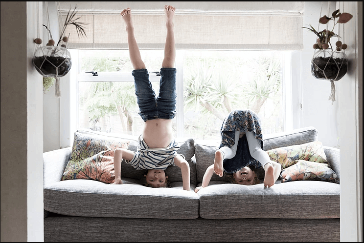 Two children playing upside down on a living room couch