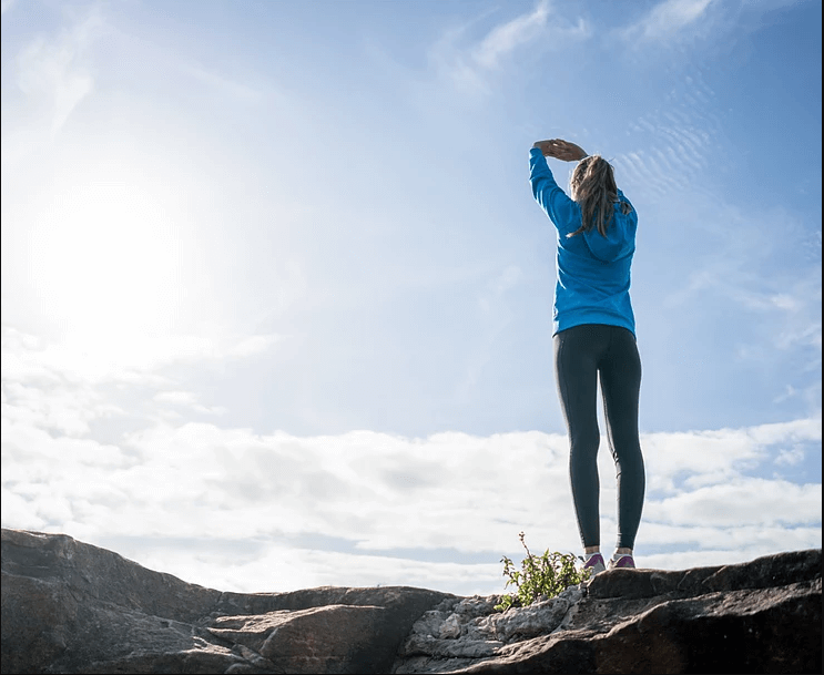 Woman stretching outdoors on a rocky ledge at sunrise