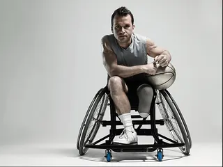 Man in a wheelchair holding a basketball on an outdoor court